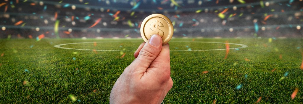 Hand holding coin in sports field with confetti falling.