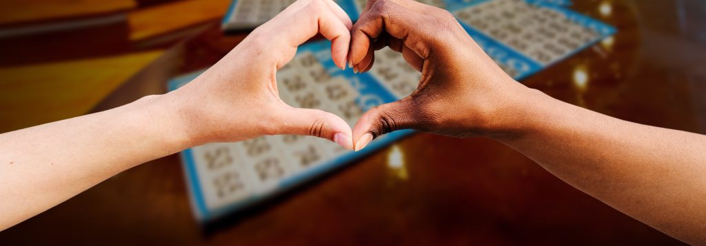 Bingo cards on table in the background. Two hands forming a heart.