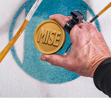 Une main tient une rondelle de hockey ressemblant à une pièce de monnaie. Le mot « mise » est inscrit sur la rondelle qui est sur le point d’être mise en jeu.
