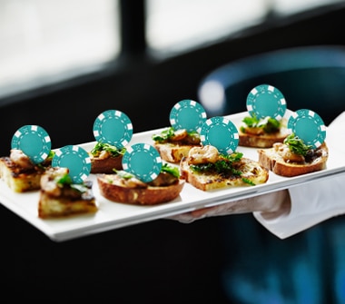 Hand holding tray of hors d'oeuvres topped with casino chips.