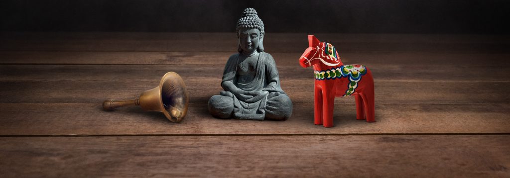 A bell, buddha statue, and wooden horse on top of table.